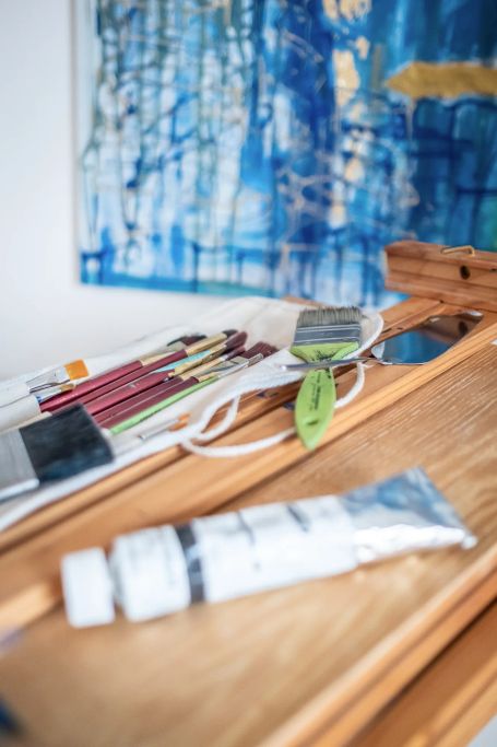 Pinsel und Farben auf einer Holzstaffelei, unscharfes Bild im Hintergrund – Kunst & Gespräche