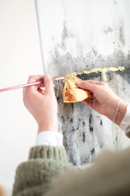 Hände tragen Blattgold mit Pinsel auf eine Leinwand auf – Kunst & Gespräche, kreatives Malen